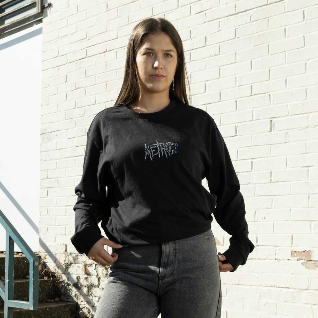 A person wearing a black Method Vortex Long Sleeve T-Shirt, standing outdoors