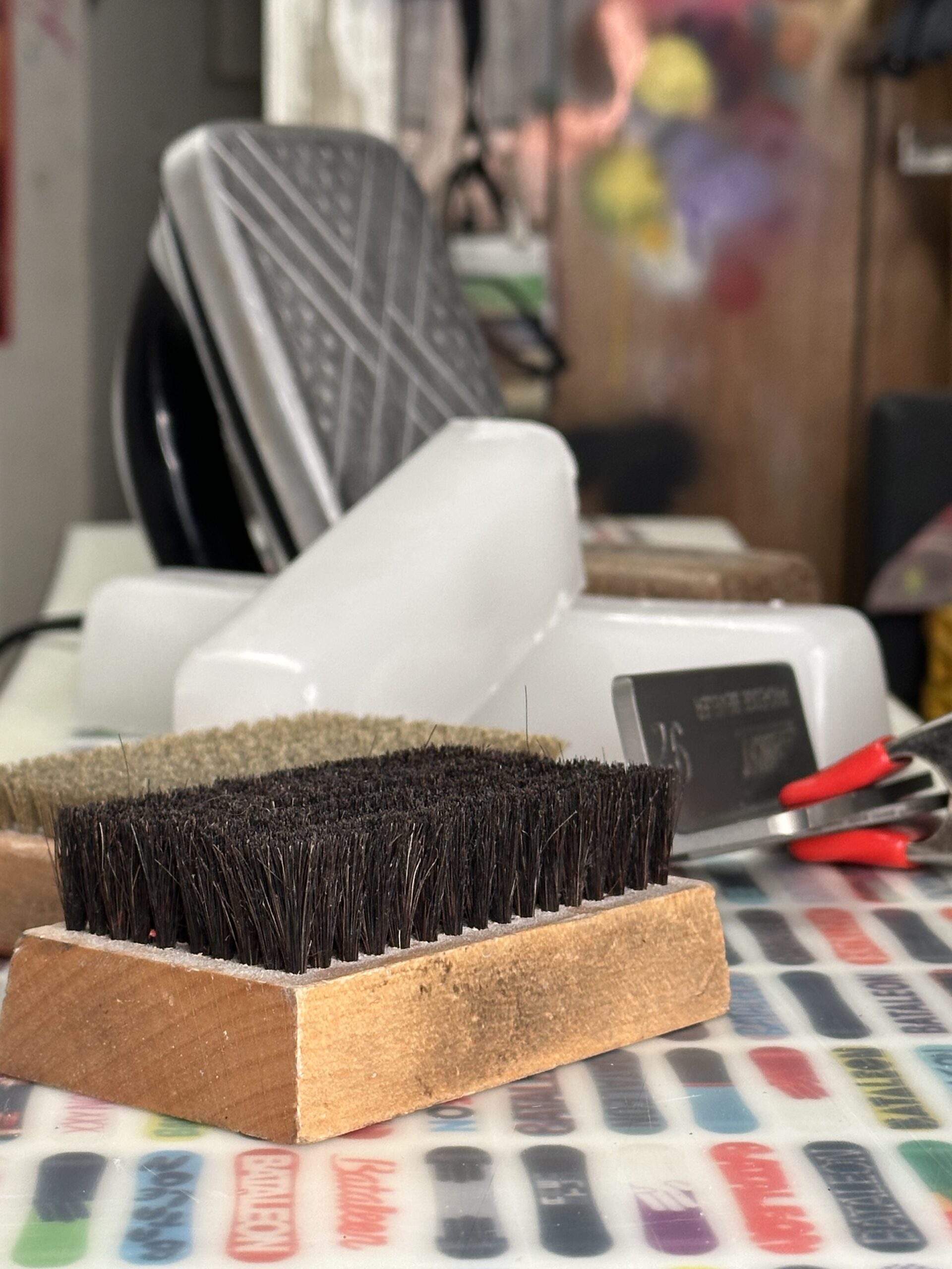 Professional snowboard hot wax service showing a waxing iron, performance wax block, and base brushes on a snowboard base